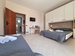Ein Hotelzimmer mit zwei Betten, einem Schreibtisch mit Computer, einem Fernseher und einem Kleiderschrank.
