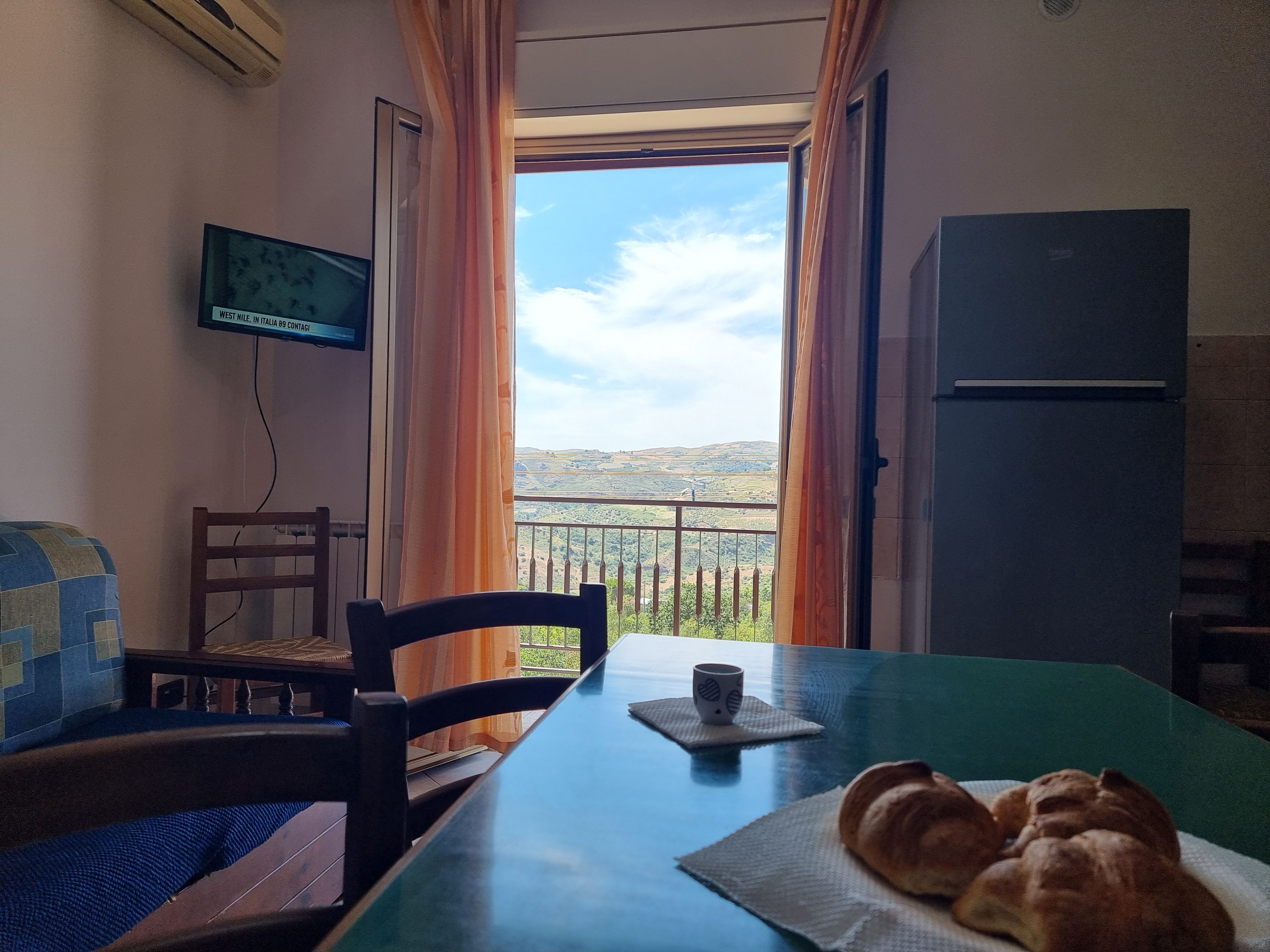 A room with a table, chairs, a television, and a view of the countryside.