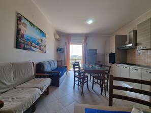 Ein Wohnzimmer mit einer Couch, einem Esstisch mit Stühlen, einer Küche mit Schränken und einem Herd sowie einem Gemälde an der Wand.