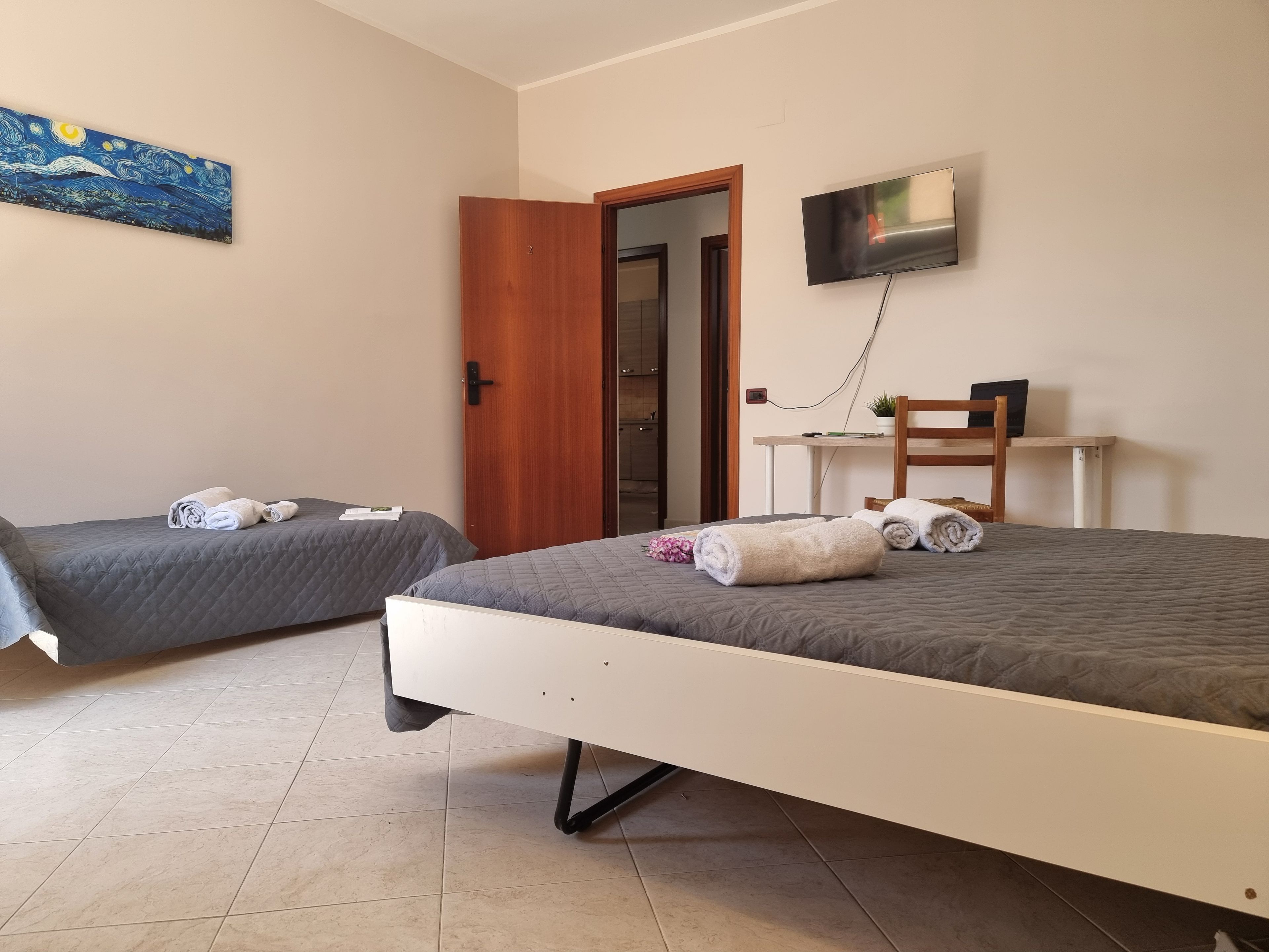 A hotel room with two beds, a desk, a TV, and a painting on the wall.