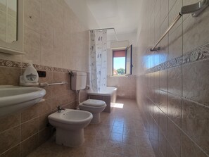 Ein Badezimmer mit Toilette, Bidet und Waschbecken, mit gefliesten Wänden und einem Fenster.