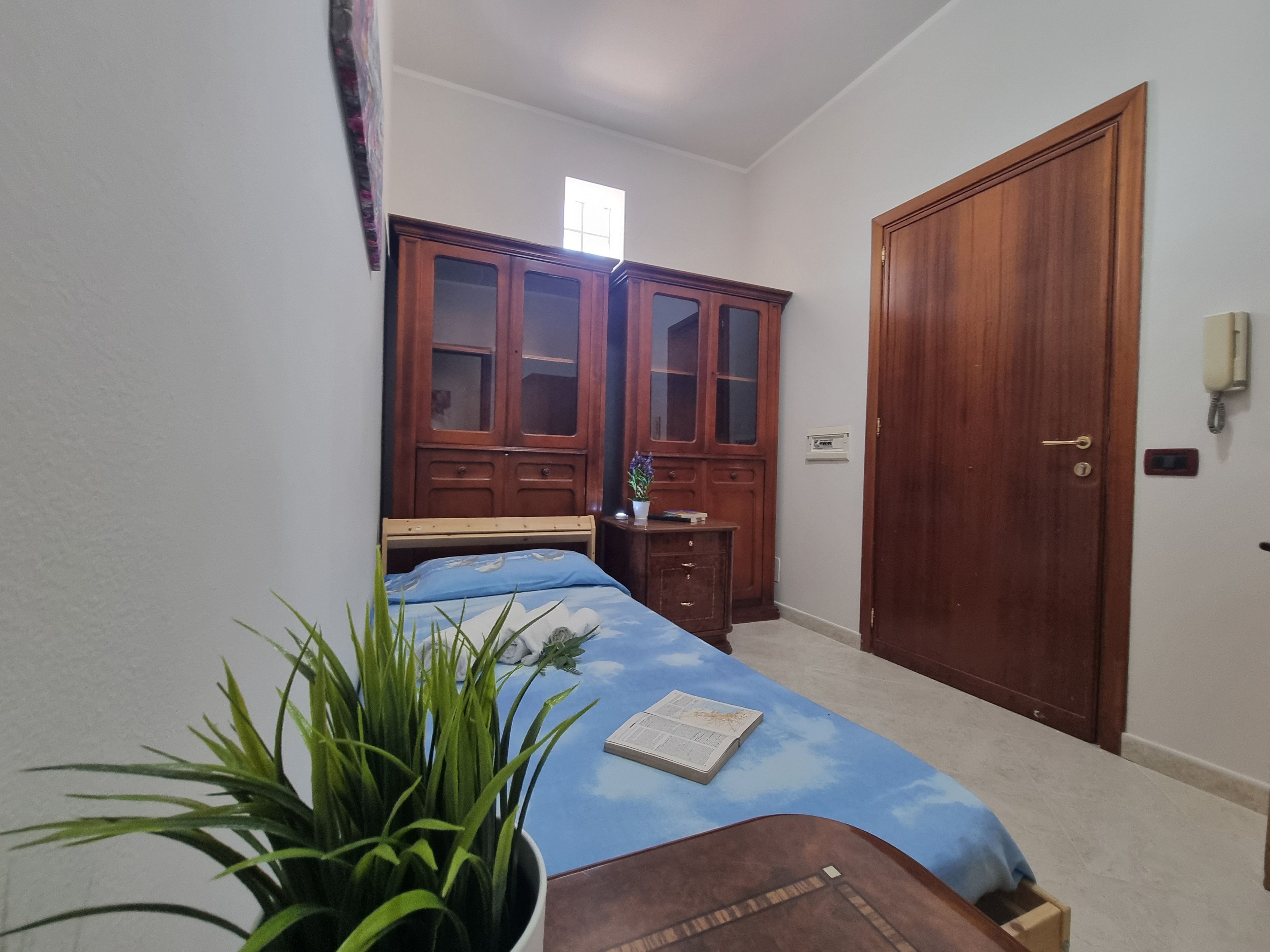 Un dormitorio con una cama, un armario de madera, una mesita de noche y una planta en maceta.