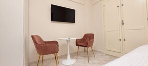 Hotellihuone, jossa on sänky, seinälle asennettu televisio ja kaksi tuolia pienen pyöreän pöydän ympärillä.