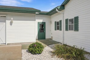 A white building with a green door and windows, a small garden area with gravel and plants, and a light fixture on the wall. - Lake and Trailside Ranch house in rural Augusta (Augusta)