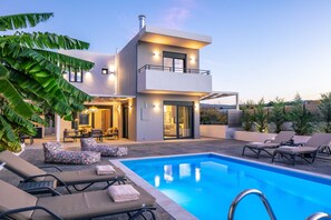 A modern two-story house with a swimming pool, outdoor seating, and a well-lit interior. - Queen Bee Villa in Prinos (Rethymno)