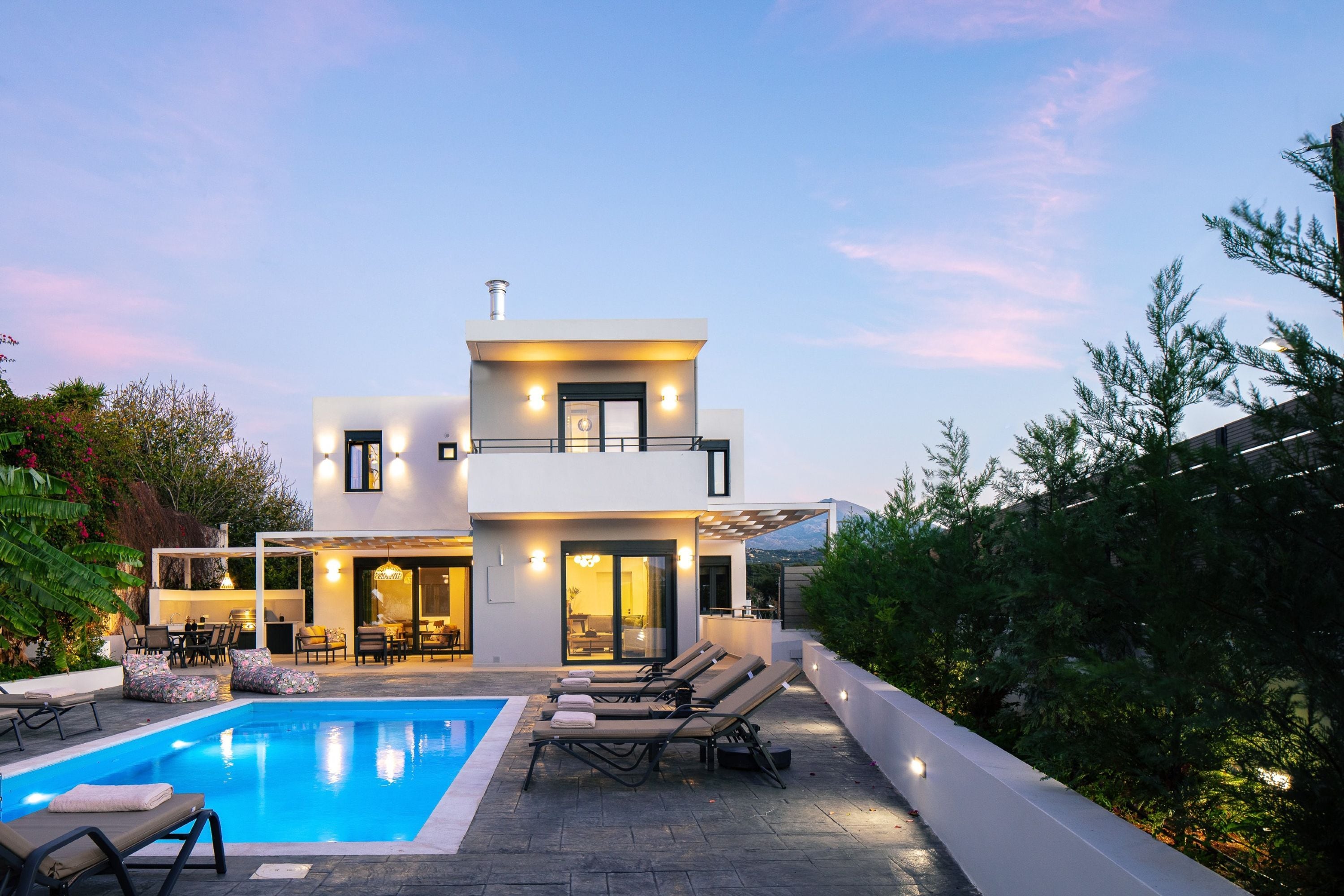 A modern two-story house with a swimming pool, outdoor seating, and a view of the mountains.