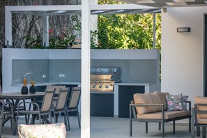 An outdoor kitchen area with a grill, dining table, and chairs. - Queen Bee Villa in Prinos (Rethymno)