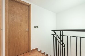 Eine Holztür mit einem Metallgriff, eine weiße Wand und ein schwarzes Metalltreppengeländer.