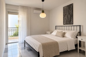 A bedroom with a bed, bedside tables, a hanging light fixture, a window with curtains, and an air conditioning unit. - Luesh ΙΙ · Large 2BR Apt | Walk to Beach and Center (Agios Nikolaos)