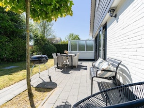 An outdoor patio with a table and chairs, a barbecue grill, a sofa, and a glass enclosure. - Holiday Home in Renesse With Swimming Pool (Renesse)