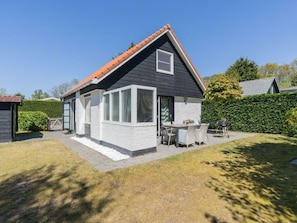 A two-story house with a black and white exterior, a red-tiled roof, and a patio with outdoor furniture. - Holiday Home in Renesse With Swimming Pool (Renesse)