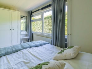 A bedroom with a bed, a radiator, a window with curtains, and a white wardrobe. - Holiday Home in Renesse With Swimming Pool (Renesse)