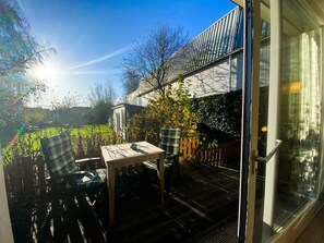 Eine Terrasse mit Tisch und Stühlen, mit Blick auf einen Garten und ein Gebäude.