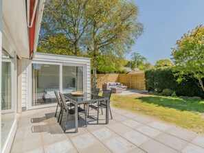 Eine moderne Außenpatio mit einem wintergartenartigen Raum, einem Esstisch mit Stühlen und einem Holzzaun.