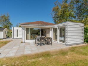 Ein modernes Haus mit einer Terrasse, einem Essbereich und einer Glastür zu einem Wohnraum.