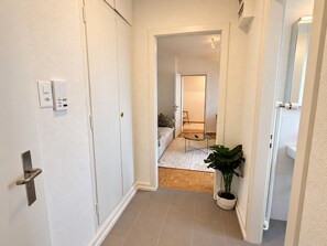 A hallway leading to a living area with a sofa, a coffee table, and a potted plant. - Stylish 1-Bedroom Apartment with a View of Zurich - Tilia 52 (Zürich)