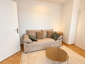 A living room with a beige sofa, a round coffee table, and a patterned rug. - Stylish 1-Bedroom Apartment with a View of Zurich - Tilia 52 (Zürich)