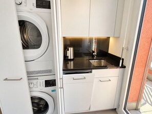 A compact kitchen with a washing machine, a kettle, and a sink. - Stylish 1-Bedroom Apartment with a View of Zurich - Tilia 52 (Zürich)