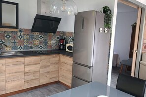 Eine Küche mit Edelstahlkühlschrank, Holzschränken, einer gefliesten Spritzschutzwand und einer Pendelleuchte.