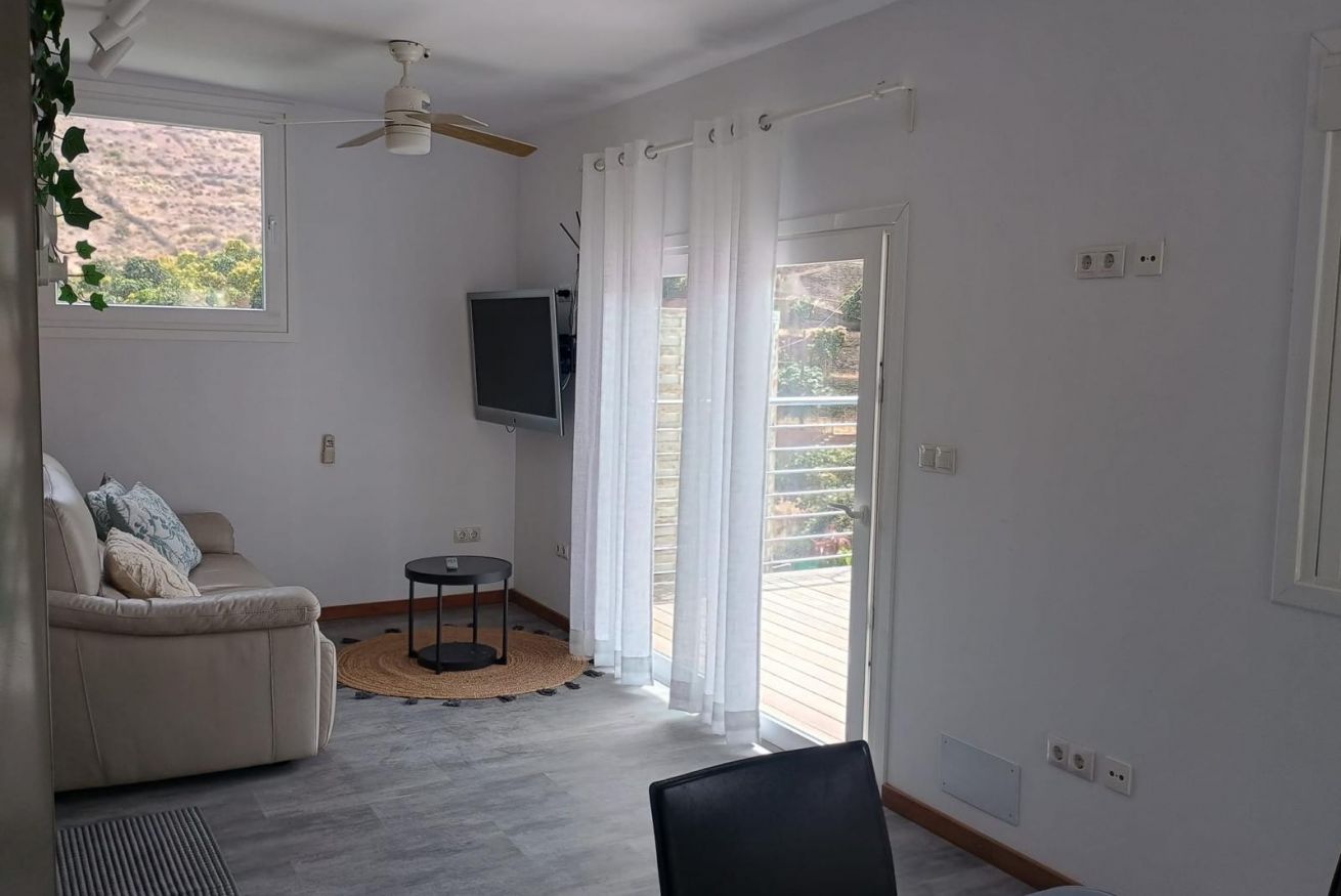 A living room with a sofa, a TV, a ceiling fan, and a sliding glass door leading to an outdoor area.