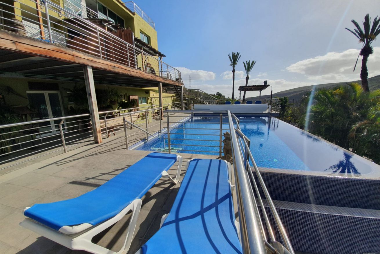 A pool area with lounge chairs, a staircase, and a building with balconies.
