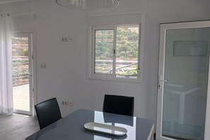 Ein Zimmer mit einem Glastisch, zwei Stühlen, einem Fenster mit Blick auf Grünflächen und einer Tür.