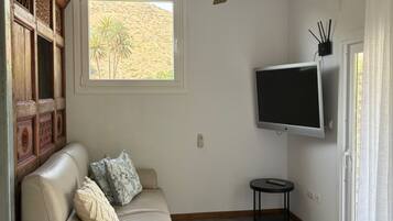 Una sala de estar con un sofá, un televisor, una mesita y una ventana con vista a palmeras.