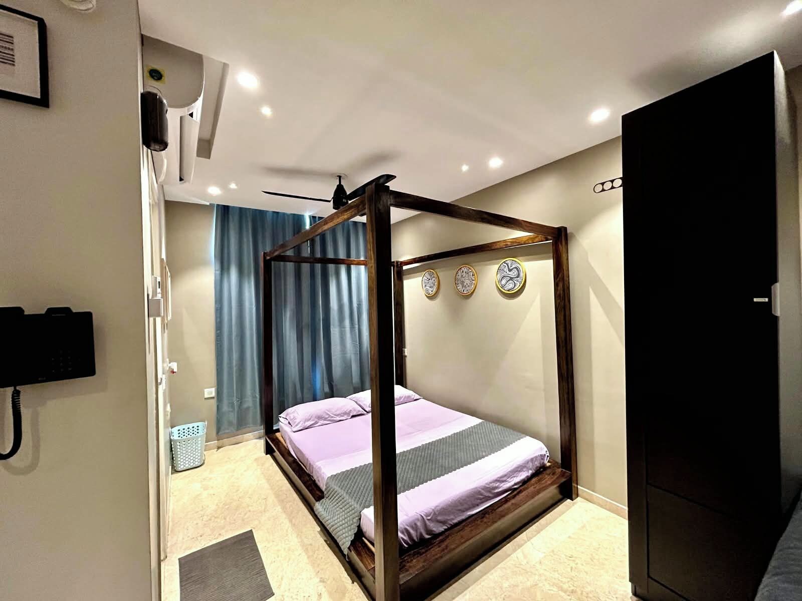 A four-poster bed with a wooden frame, a wall-mounted telephone, and a door to the right.