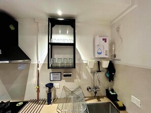 A compact kitchen with a built-in dishwasher, a stainless steel sink, and a black range hood. - Japanese Studio_Hiranandani Estate_WiFi (Thane)