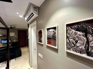 A hallway with artwork on the walls, a ceiling fan, and a door leading to another room. - Japanese Studio_Hiranandani Estate_WiFi (Thane)