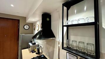A kitchen with a gas stove, a black range hood, and a shelf with glasses.