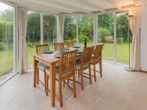 A conservatory with a dining table set for six, surrounded by chairs, and large glass doors leading to a garden. - Holiday Home in Renesse With Swimming Pool (Renesse)