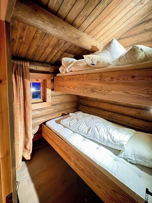 A bunk bed with wooden headboard and footboard, a window with curtains, and a view of the night sky. - Mountain farm from the 1900s with panoramic views (Geilo)
