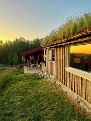 A wooden cabin with a large window, a deck, and a stone wall. - Mountain farm from the 1900s with panoramic views (Geilo)