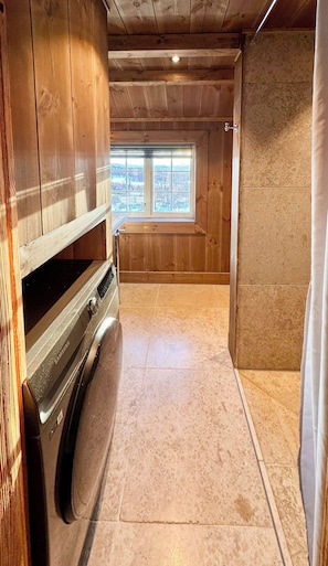A laundry room with a washing machine, wooden walls, a window with a view, and a tiled floor. - Mountain farm from the 1900s with panoramic views (Geilo)