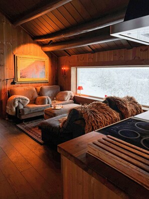 A cozy cabin interior with a wooden ceiling, a sofa set, a dining table, and a window with a view of a snowy landscape. - Mountain farm from the 1900s with panoramic views (Geilo)