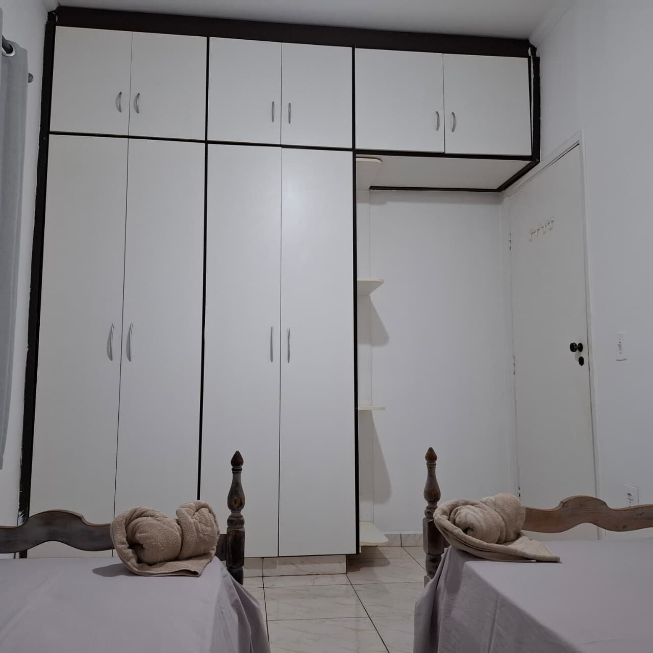 A bedroom with a large wardrobe, two beds with headboards, and a door with a handle.