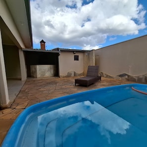 A swimming pool with a lounge chair, stone flooring, and a small building with a chimney. - CASA FRENTE 1111 (São José do Rio Preto)