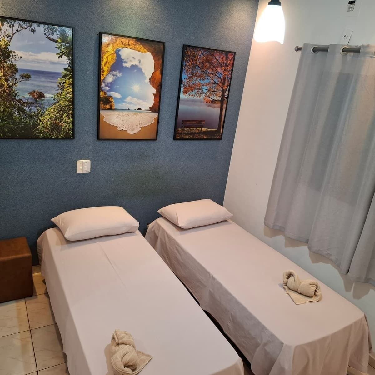 A room with two single beds, a nightstand, and a wall with three framed pictures.