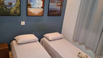 A room with two single beds, a nightstand, and a wall with three framed pictures.