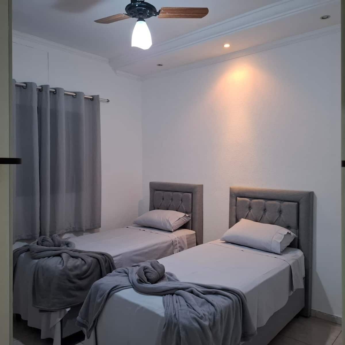 Una habitación con dos camas individuales, un ventilador de techo y una ventana con cortinas.