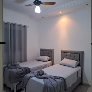 A room with two single beds, a ceiling fan, and a window with curtains. - CASA FRENTE 1111 (São José do Rio Preto)