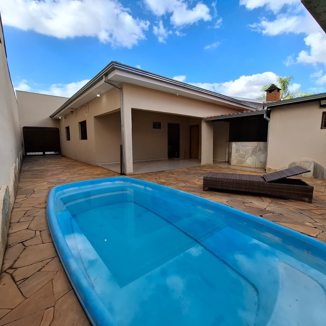 A swimming pool with a tiled deck, a covered patio area, and a building with a flat roof.