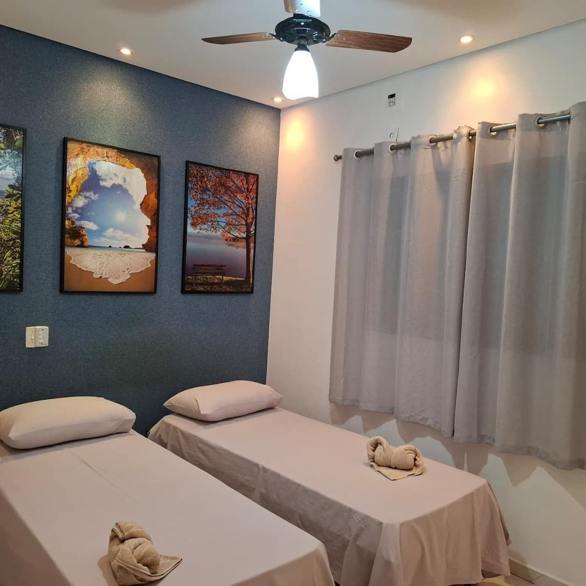 A hotel room with two beds, a ceiling fan, and artwork on the wall.