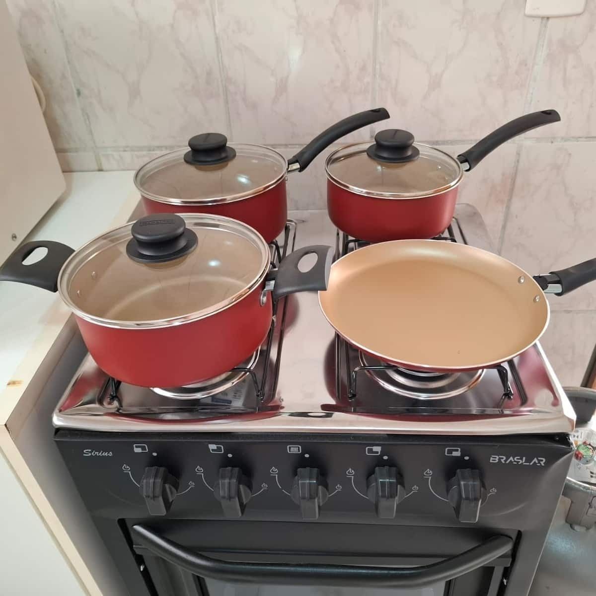 A kitchen with four red pots on a stove, a pan, and a black oven with control knobs.