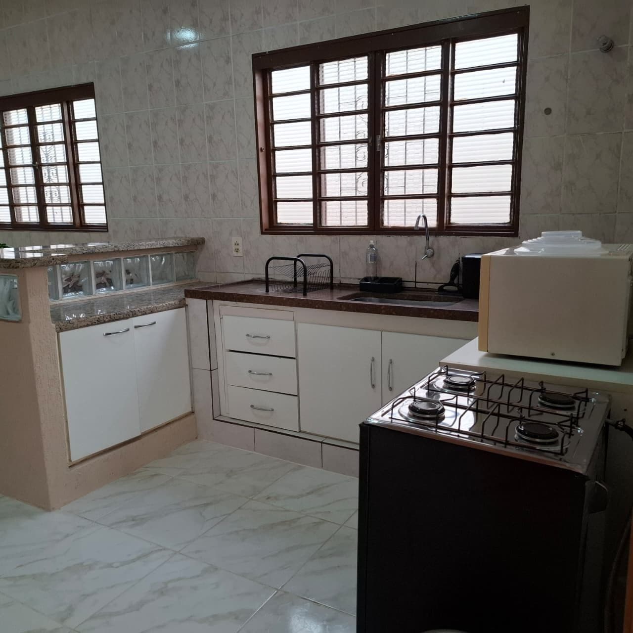 A kitchen with a gas stove, white cabinets, a window with blinds, and a countertop with a sink.