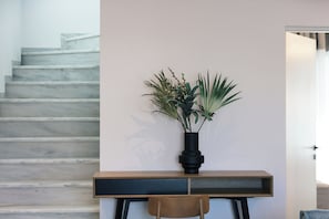 Een modern ontworpen trap, een houten bureau met een zwarte vaas met groene planten, en een stoel voor het bureau.