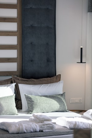 A neatly made bed with pillows and a folded towel, a dark upholstered headboard, and a simple bedside lamp. - Queen Bee Villa - Four Bedroom Villa, Sleeps 10 (Prinos)
