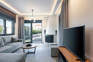 A modern living room with a sofa, coffee table, TV, fireplace, and large windows. - Queen Bee Villa - Four Bedroom Villa, Sleeps 10 (Prinos)