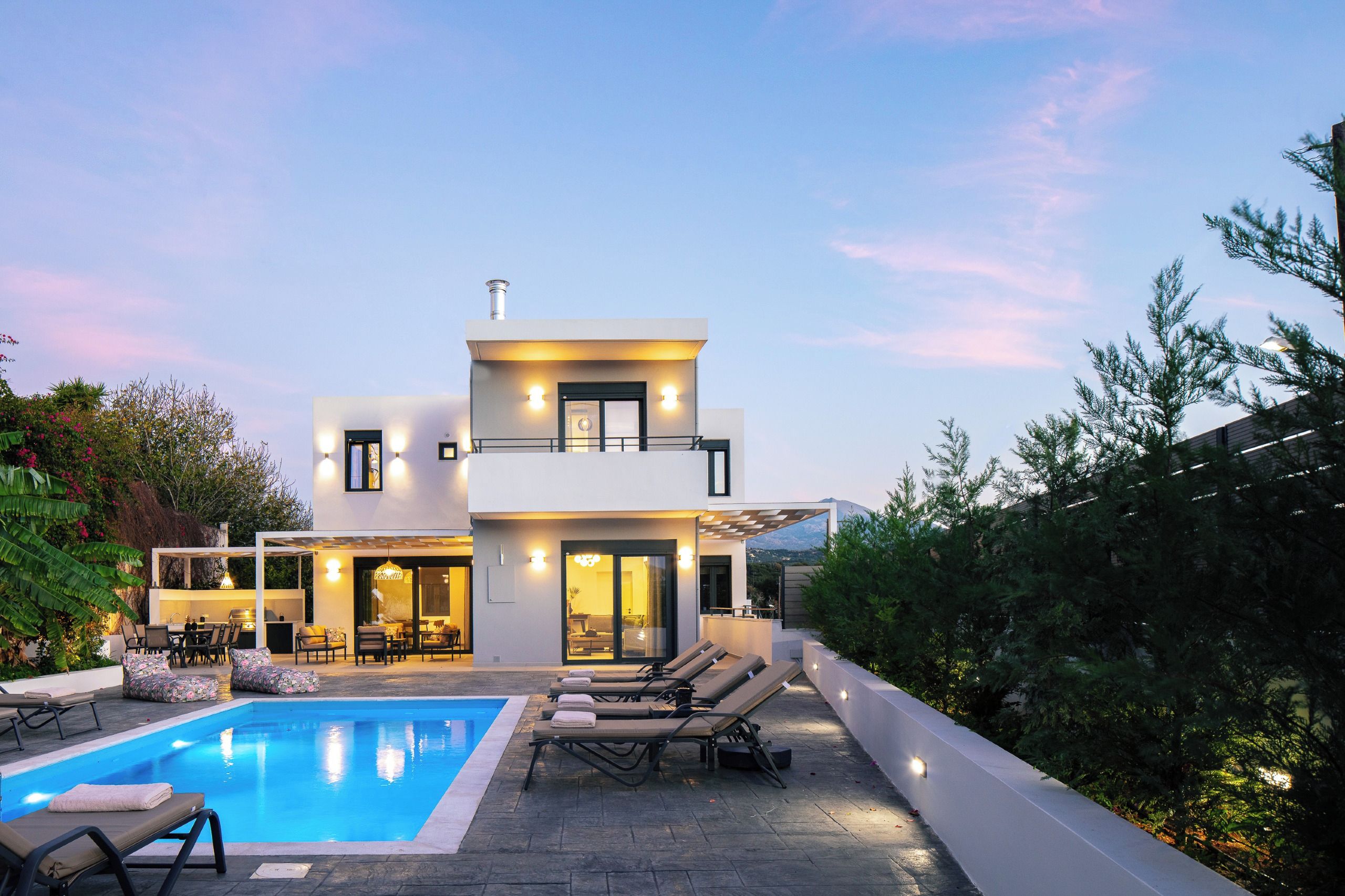 A modern two-story house with a swimming pool, outdoor seating, and a view of the mountains.